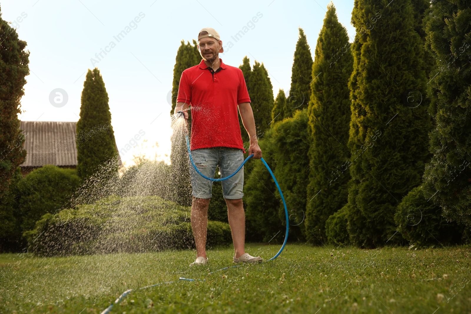 Photo of Man watering lawn with hose in backyard