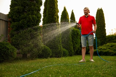 Photo of Man watering lawn with hose in backyard