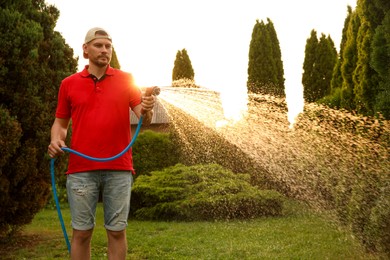 Man watering lawn with hose in backyard on sunny day