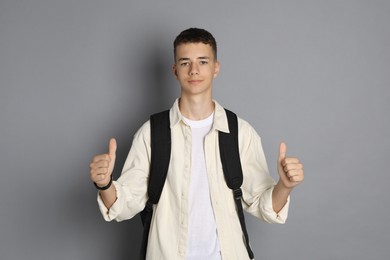 Portrait of teenage boy with backpack showing thumbs up on grey background