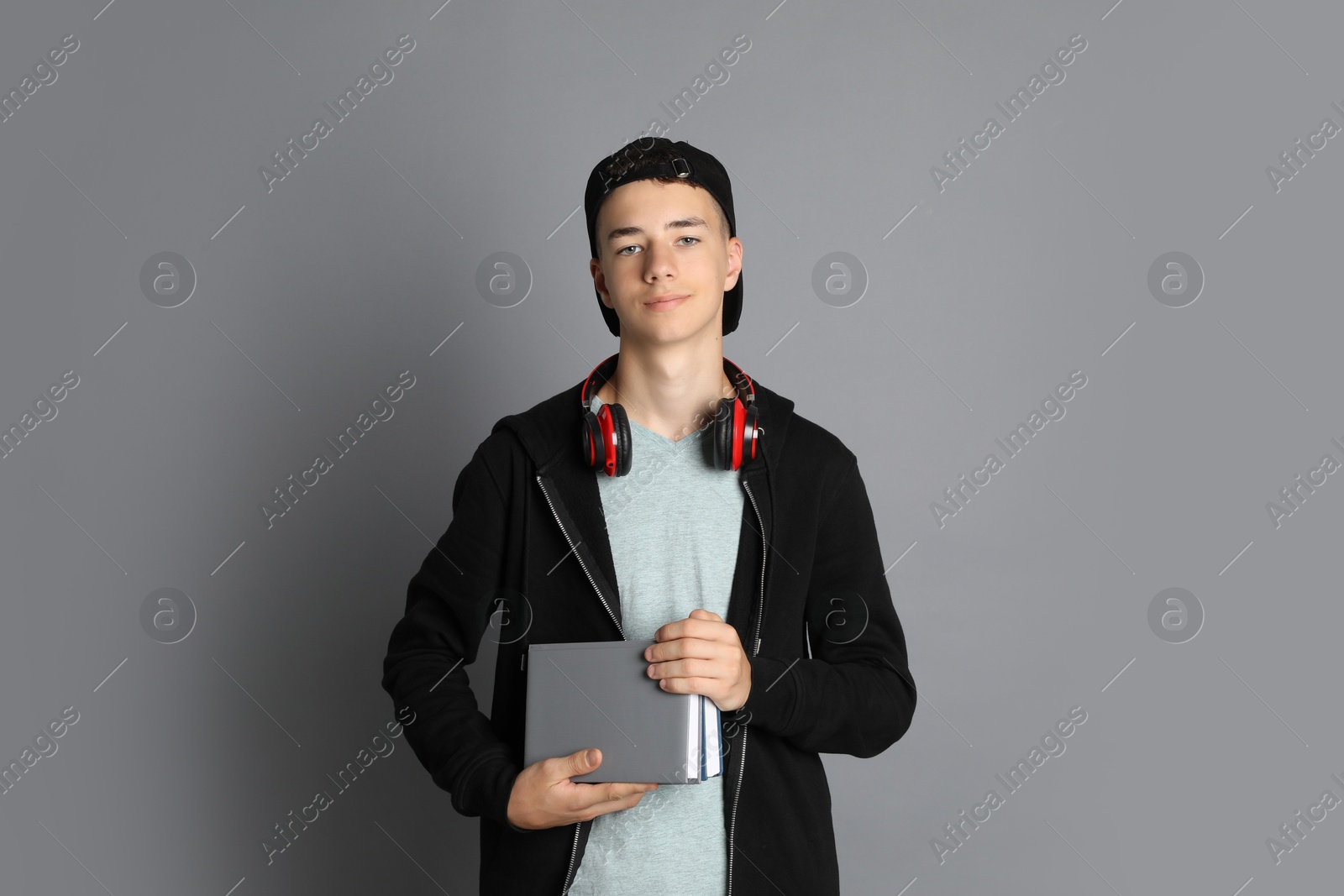 Photo of Portrait of teenage boy with headphones and books on grey background