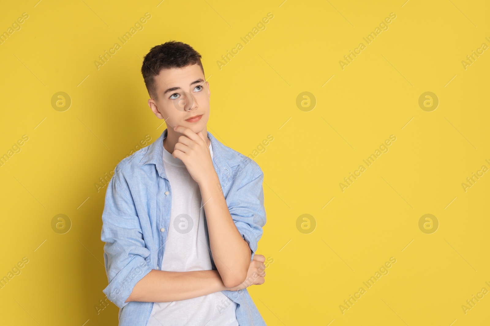 Photo of Portrait of thoughtful teenage boy on yellow background, space for text