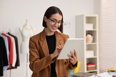 Photo of Happy fashion designer using tablet in workshop