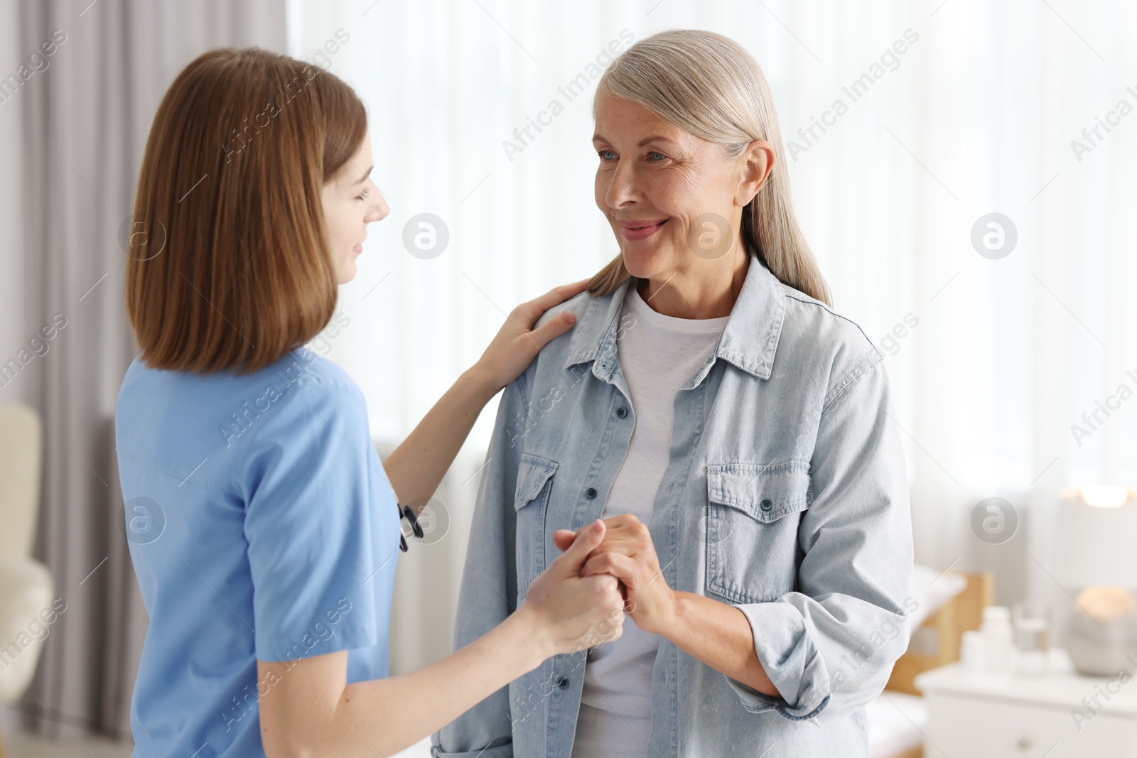 Photo of Young healthcare worker supporting senior patient indoors