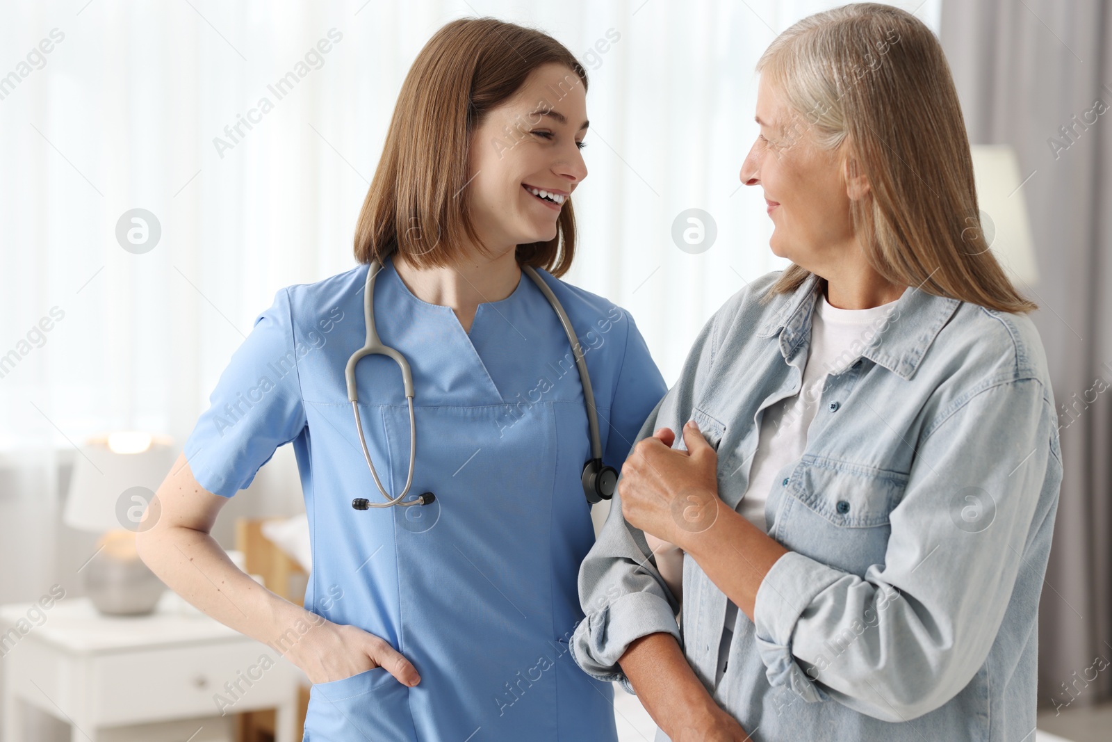 Photo of Smiling healthcare worker supporting senior patient indoors