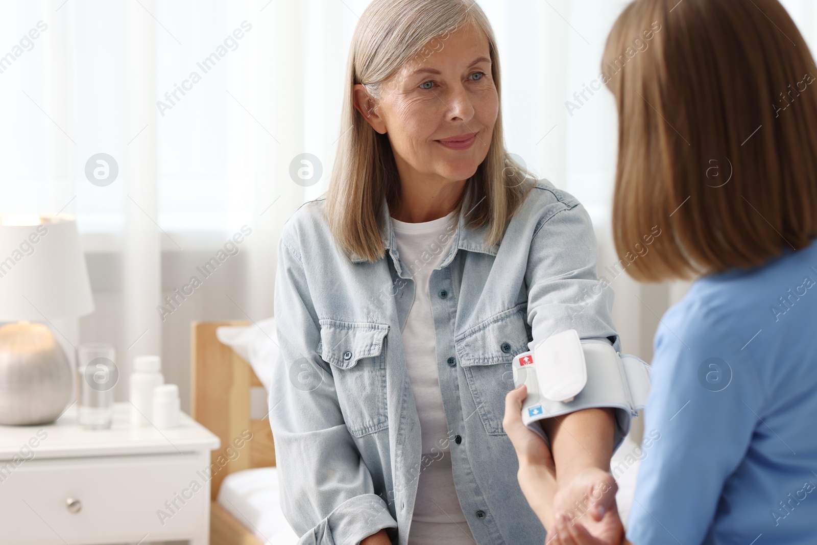 Photo of Healthcare worker measuring patient's blood pressure indoors. Space for text