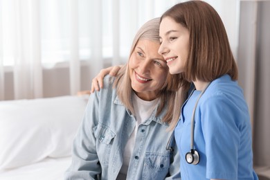 Photo of Smiling healthcare worker supporting senior patient on bed indoors. Space for text