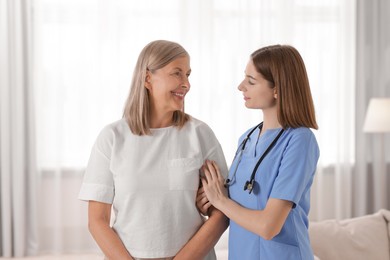 Photo of Young healthcare worker supporting senior patient indoors