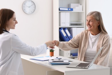 Smiling healthcare worker shaking hands with senior patient in hospital