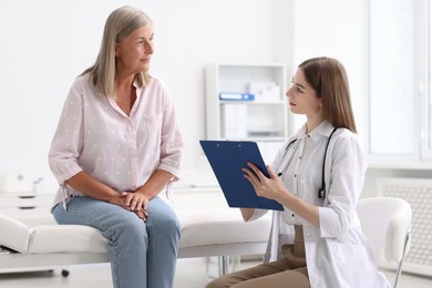 Young healthcare worker with clipboard consulting senior patient in hospital