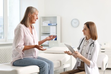 Photo of Smiling healthcare worker with tablet consulting senior patient in hospital