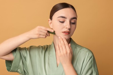 Photo of Beautiful young woman doing facial massage with gua sha tool on beige background