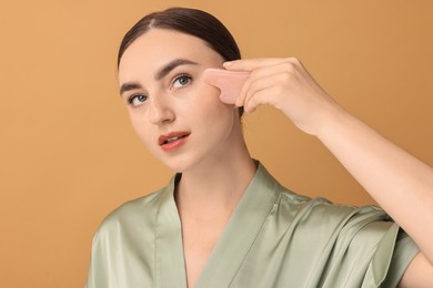 Photo of Beautiful young woman doing facial massage with gua sha tool on beige background