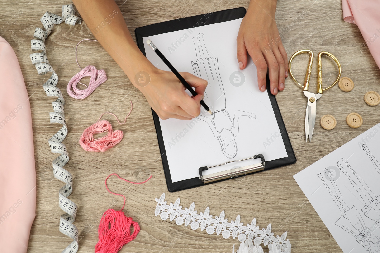 Photo of Fashion designer drawing sketch of stylish dress at wooden table, top view