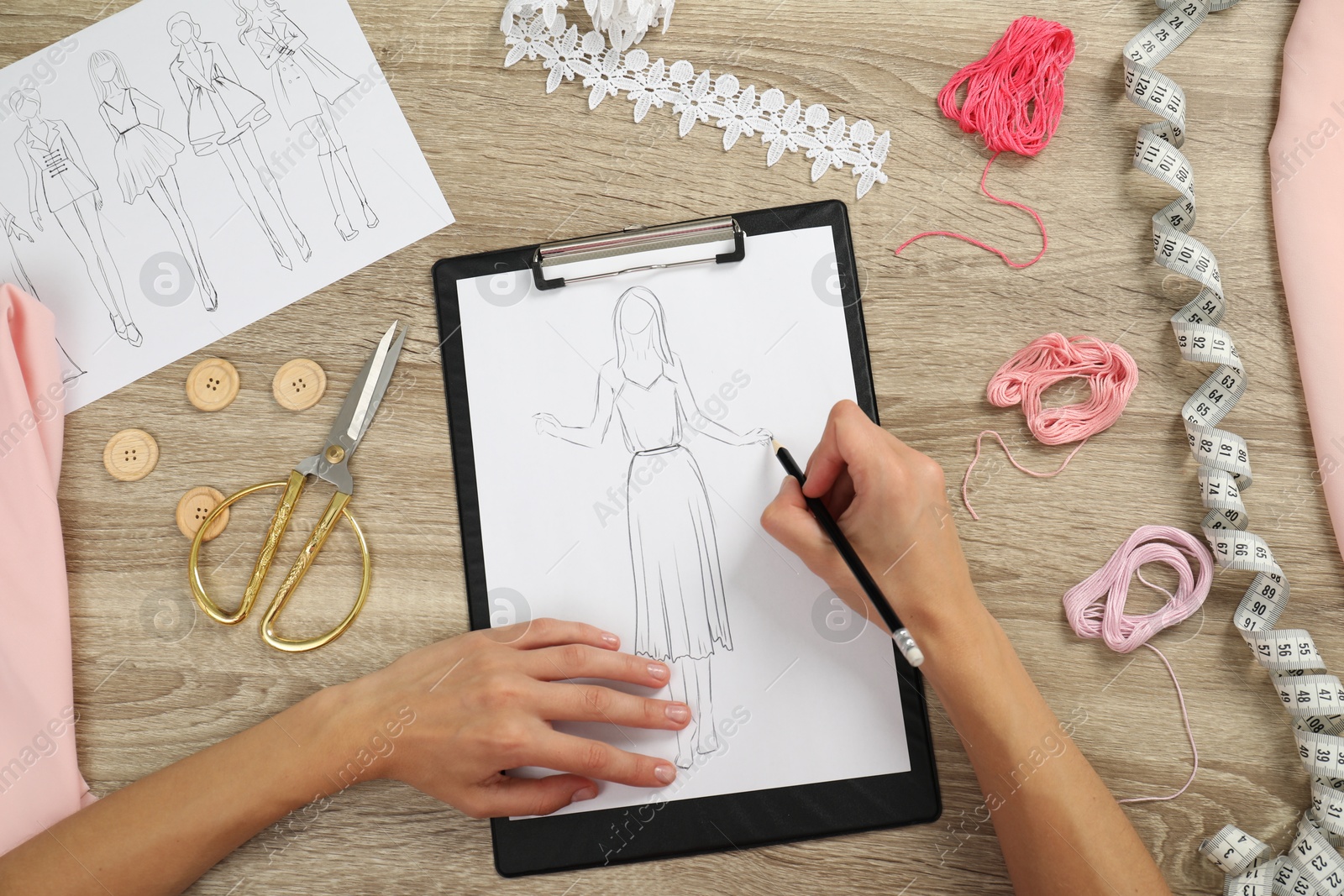 Photo of Fashion designer drawing sketch of stylish dress at wooden table, top view