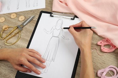 Photo of Fashion designer drawing sketch of stylish dress at wooden table, closeup