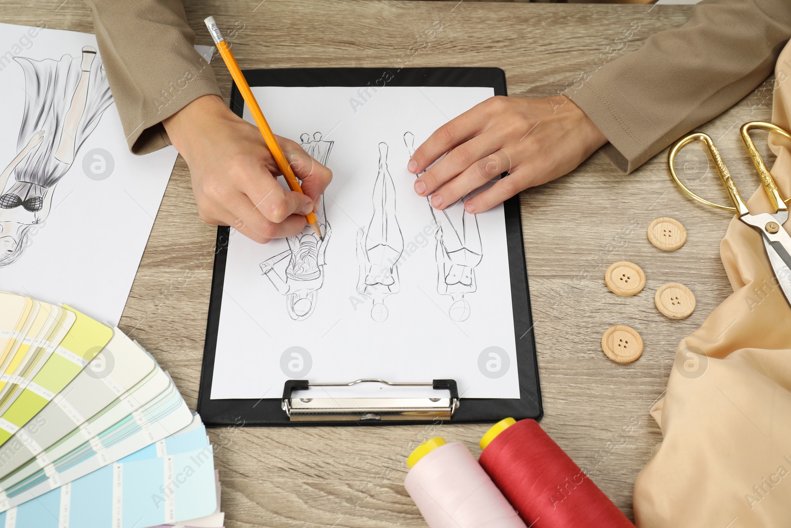 Photo of Fashion designer drawing sketch of stylish clothes at wooden table, closeup