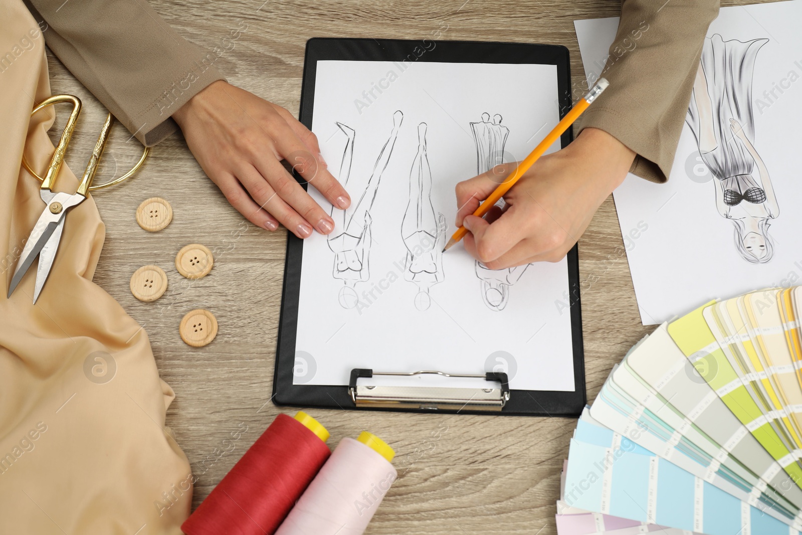 Photo of Fashion designer drawing sketch of stylish clothes at wooden table