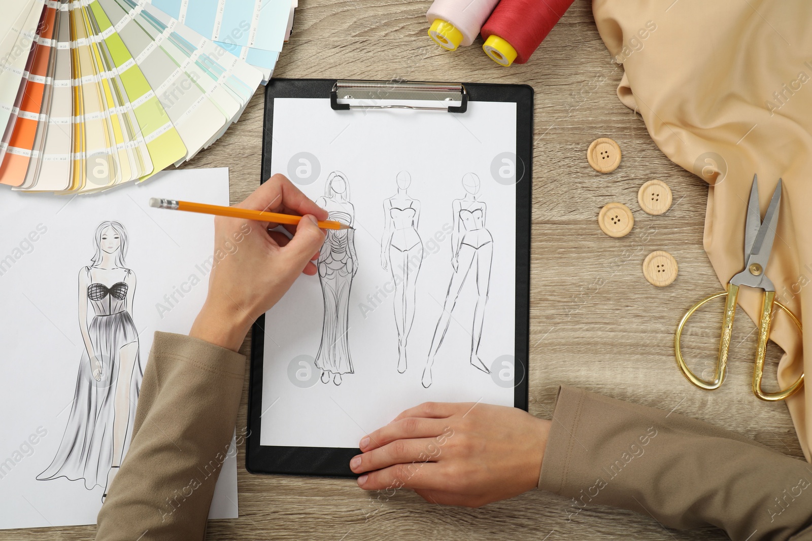 Photo of Fashion designer drawing sketch of stylish clothes at wooden table, top view