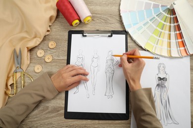 Photo of Fashion designer drawing sketch of stylish clothes at wooden table, top view