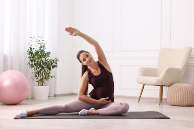 Photo of Beautiful pregnant woman doing stretching exercises on mat at home