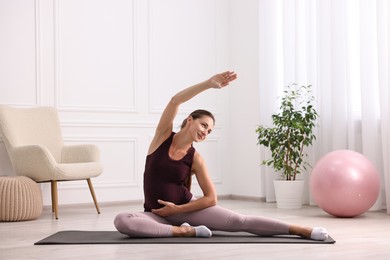 Photo of Beautiful pregnant woman doing stretching exercises on mat at home