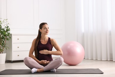 Beautiful pregnant woman with fitball on exercise mat at home