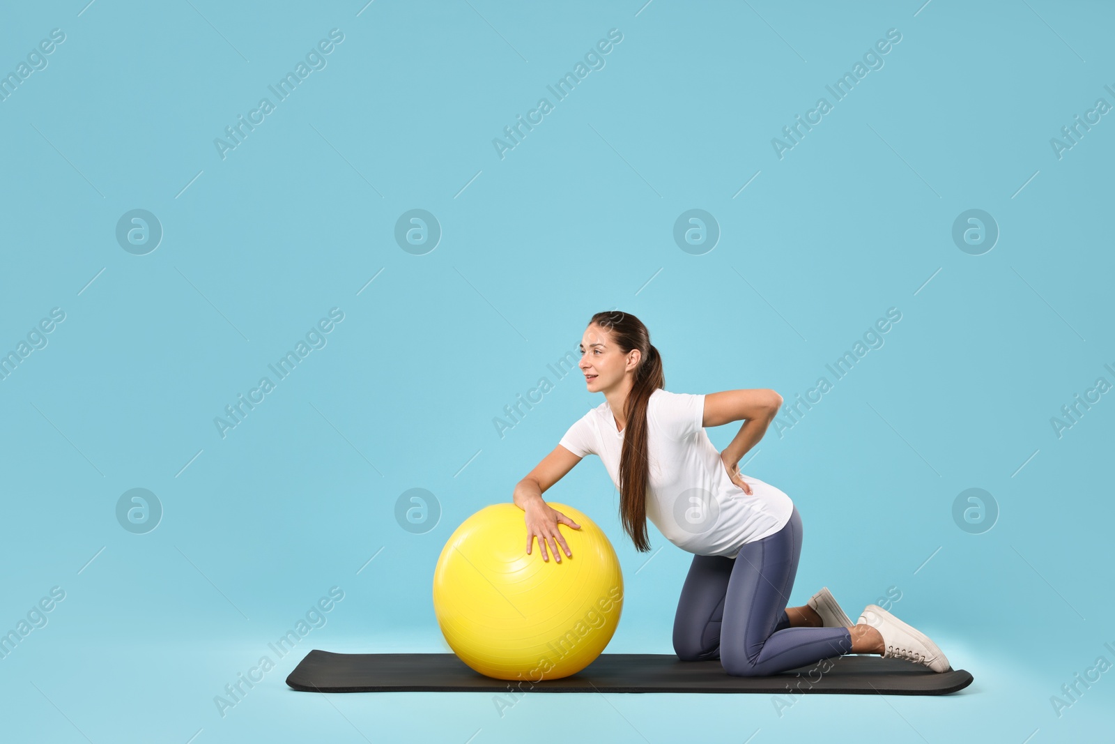 Photo of Beautiful pregnant woman doing exercises with fitball on mat against light blue background