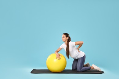 Photo of Beautiful pregnant woman doing exercises with fitball on mat against light blue background