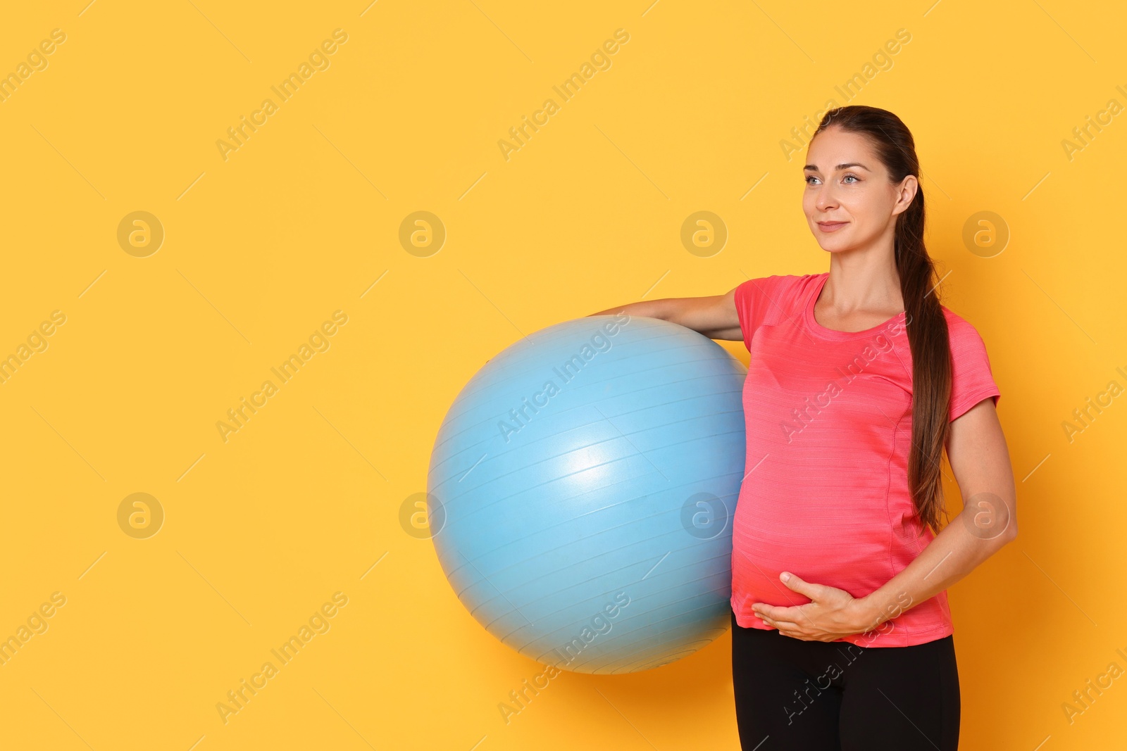 Photo of Beautiful pregnant woman with fitball on yellow background, space for text