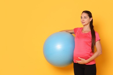 Beautiful pregnant woman with fitball on yellow background, space for text