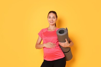 Photo of Beautiful pregnant woman with exercise mat on yellow background