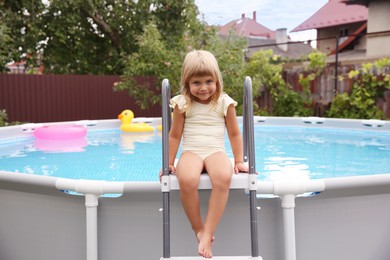 Photo of Little girl sitting on swimming pool ladder outdoors