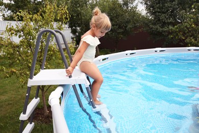 Little girl getting into swimming pool by ladder outdoors