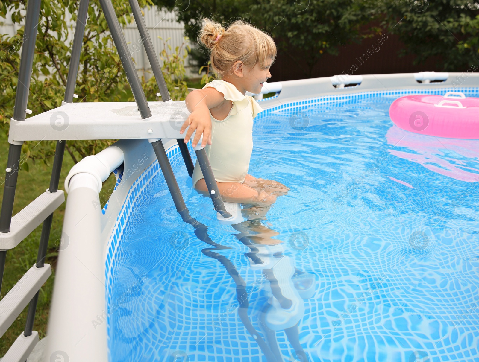 Photo of Little girl getting into swimming pool by ladder outdoors