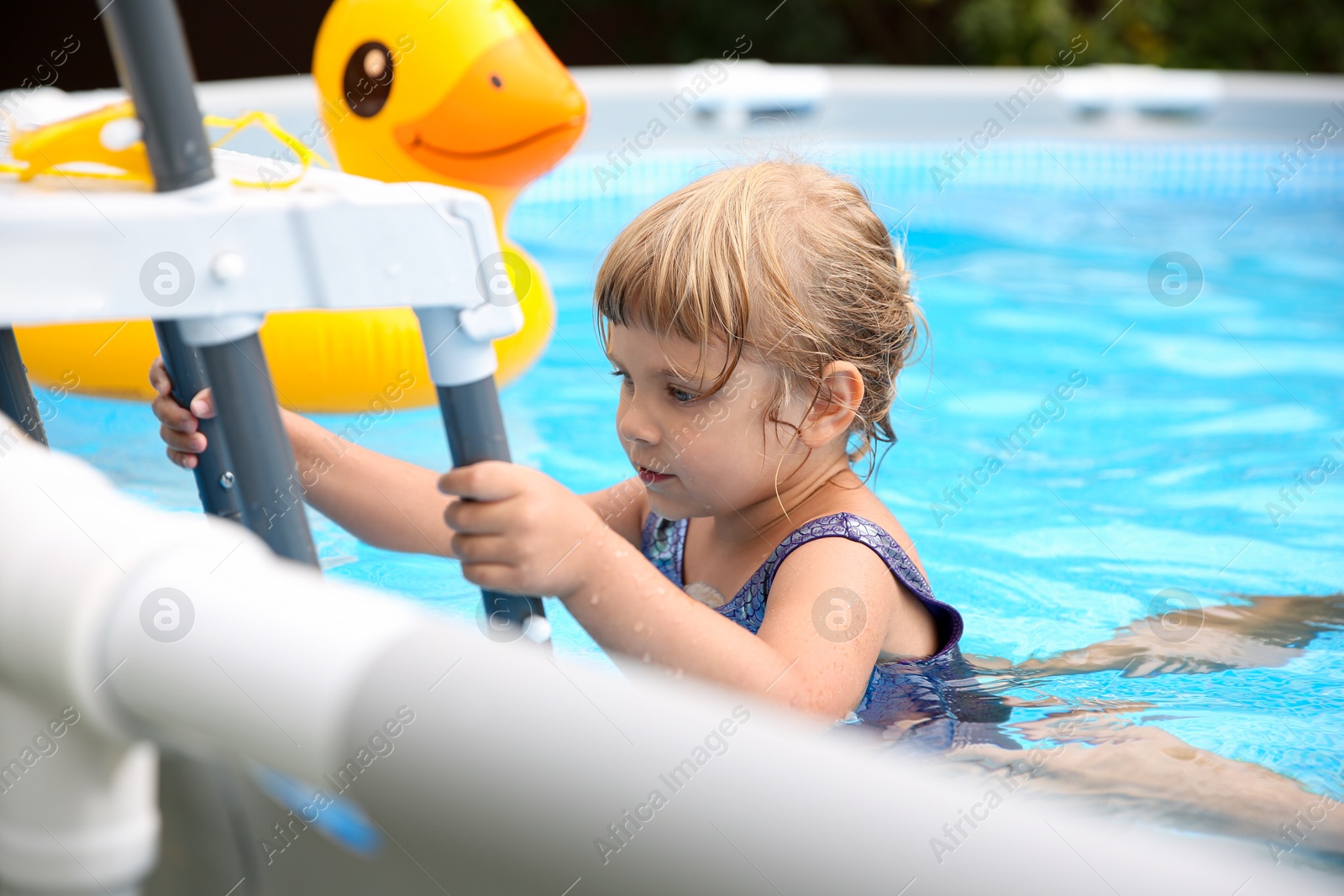 Photo of Little girl getting out of swimming pool by ladder outdoors