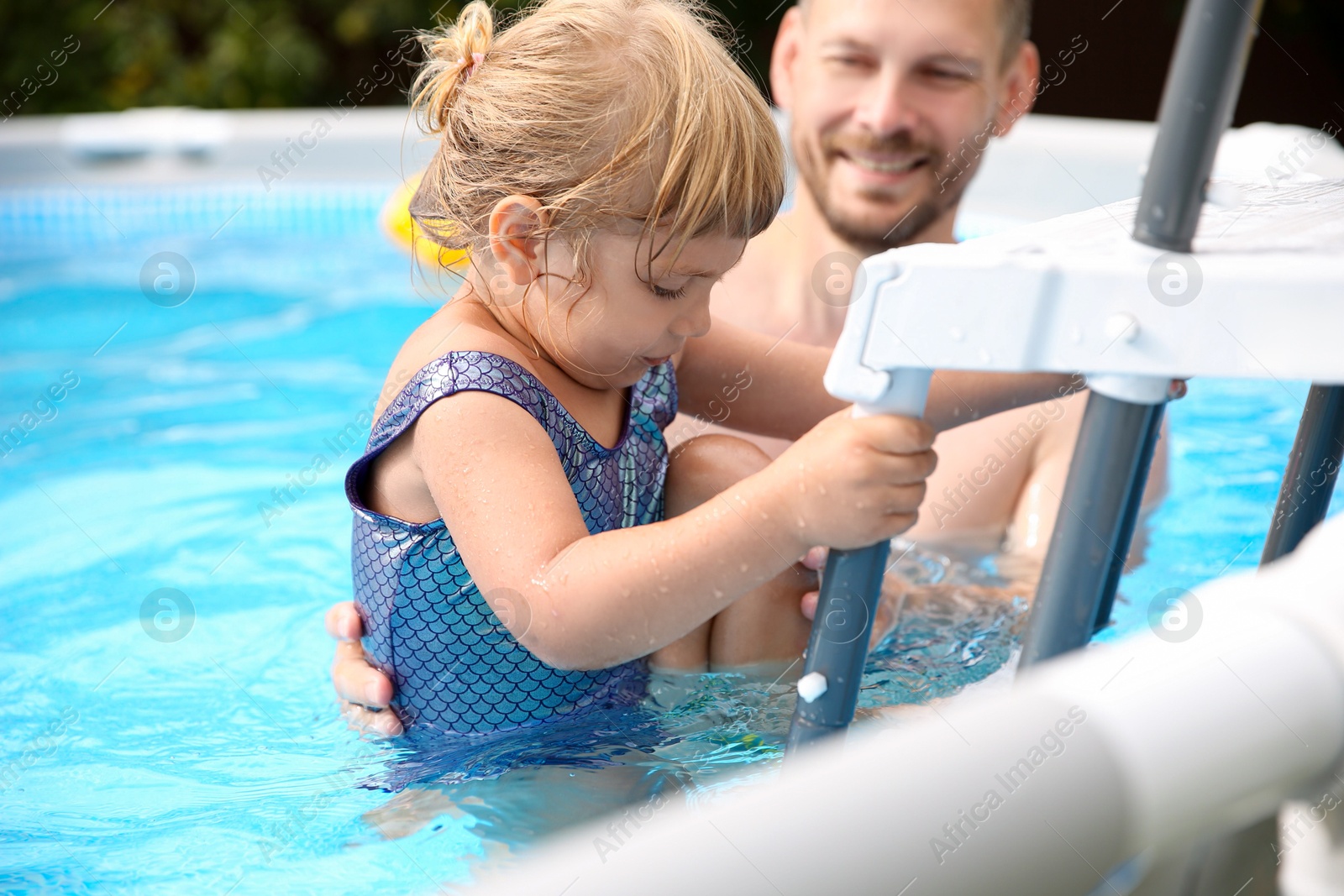 Photo of Little girl getting out of swimming pool by ladder outdoors