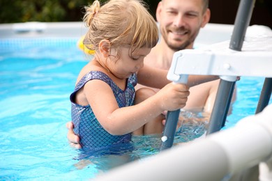 Photo of Little girl getting out of swimming pool by ladder outdoors