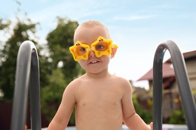 Photo of Little boy getting out of swimming pool by ladder outdoors