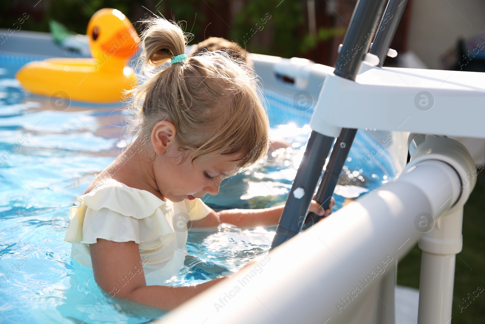 Photo of Little girl getting out of swimming pool by ladder outdoors