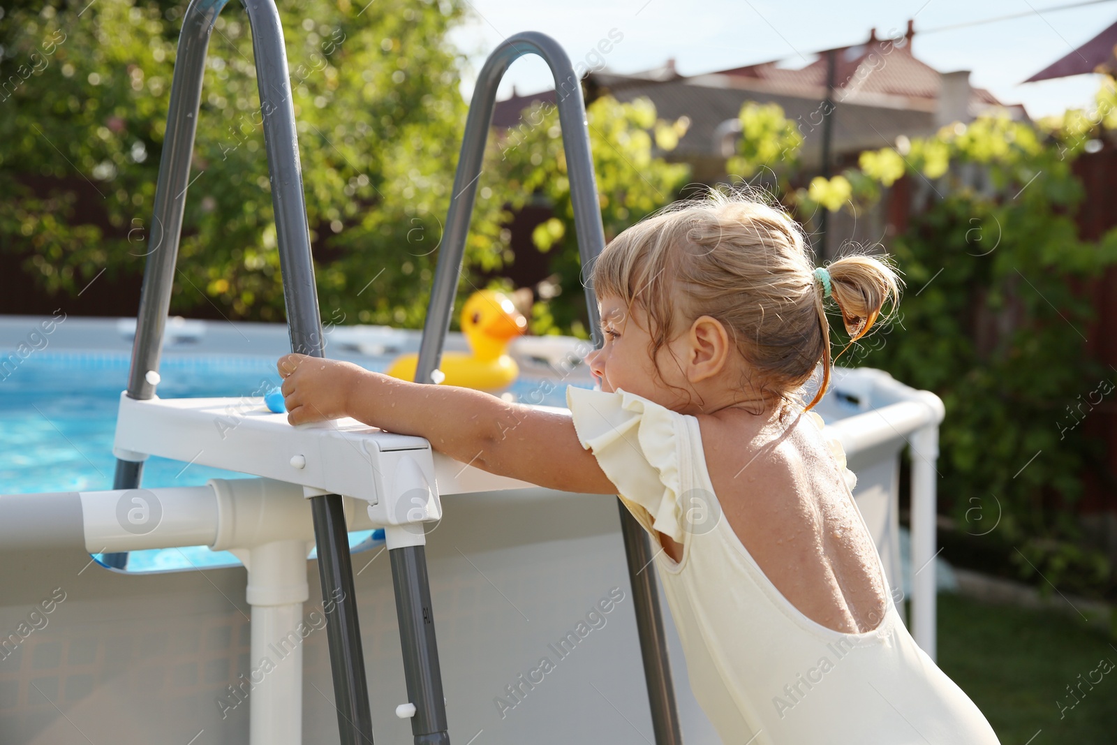 Photo of Little girl getting out of swimming pool by ladder outdoors