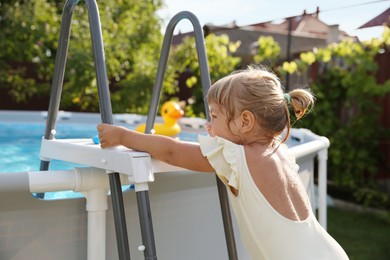 Little girl getting out of swimming pool by ladder outdoors