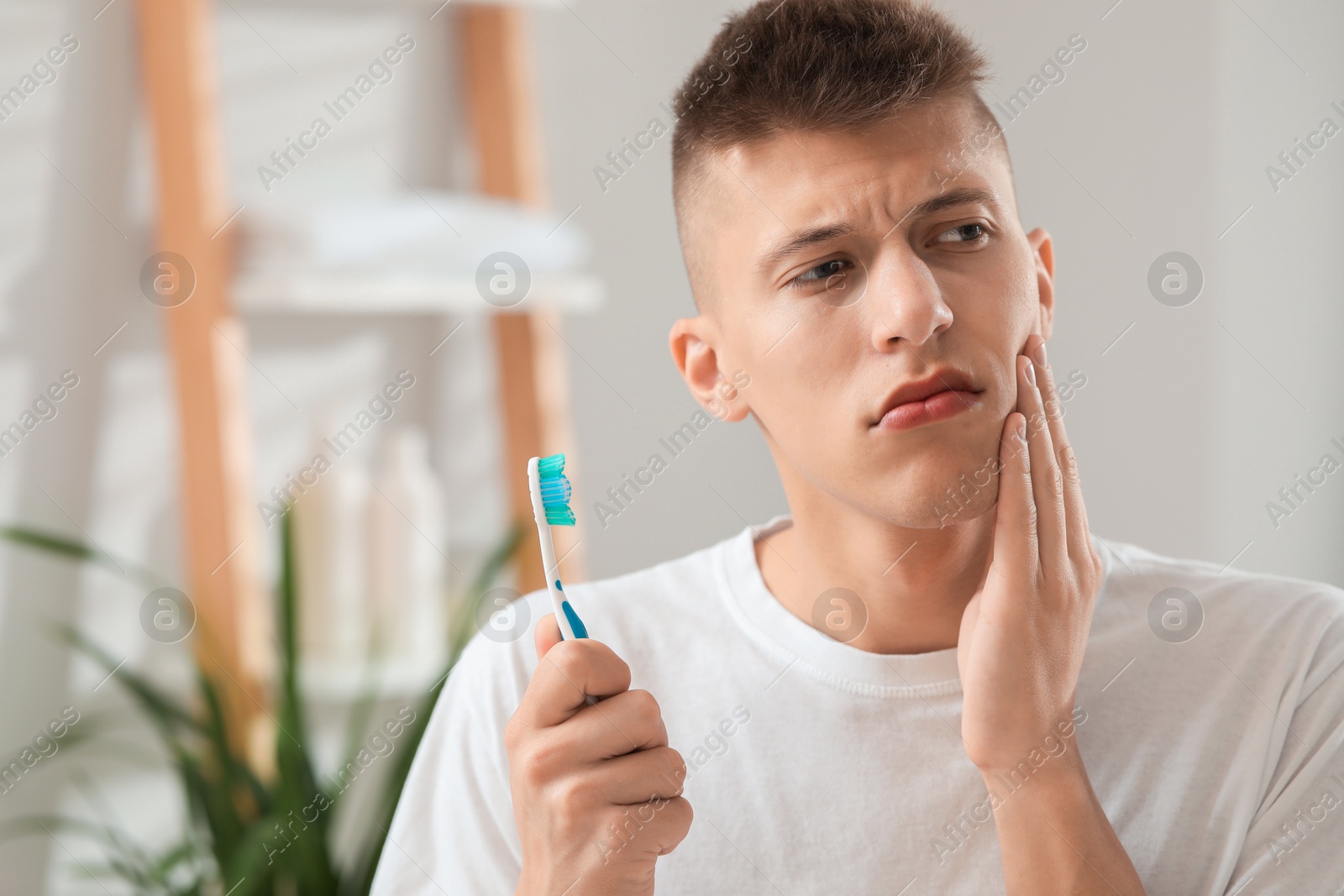 Photo of Young man with toothbrush suffering from toothache in bathroom