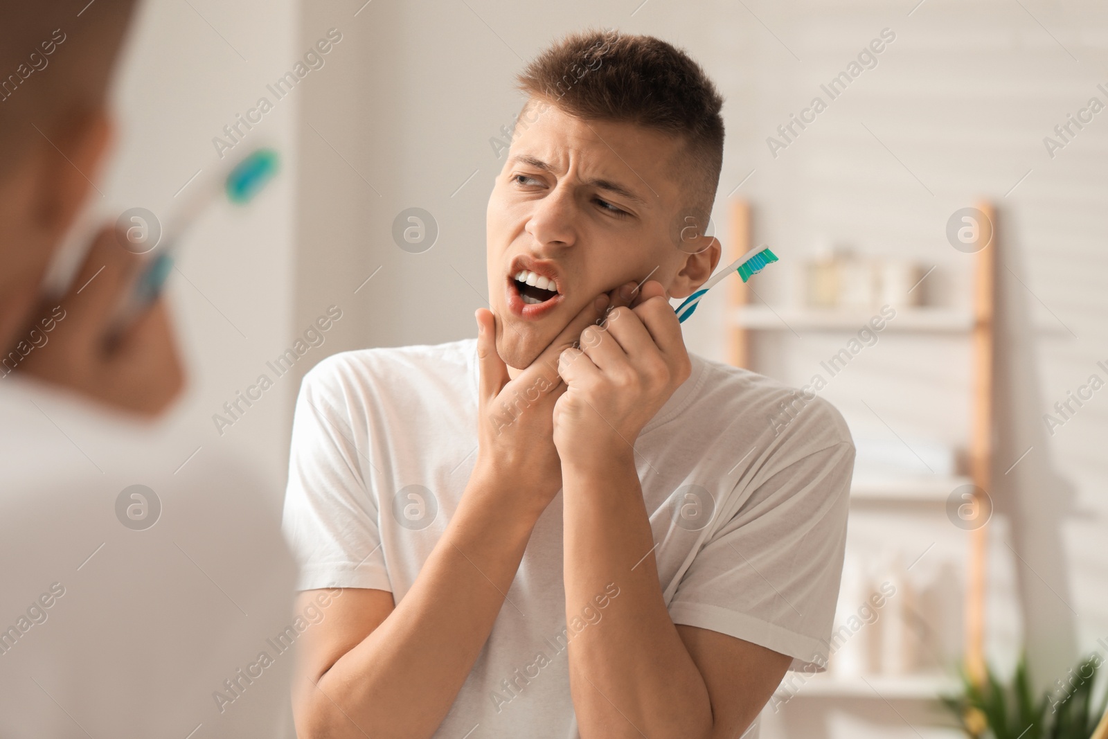 Photo of Young man with toothbrush suffering from toothache in bathroom