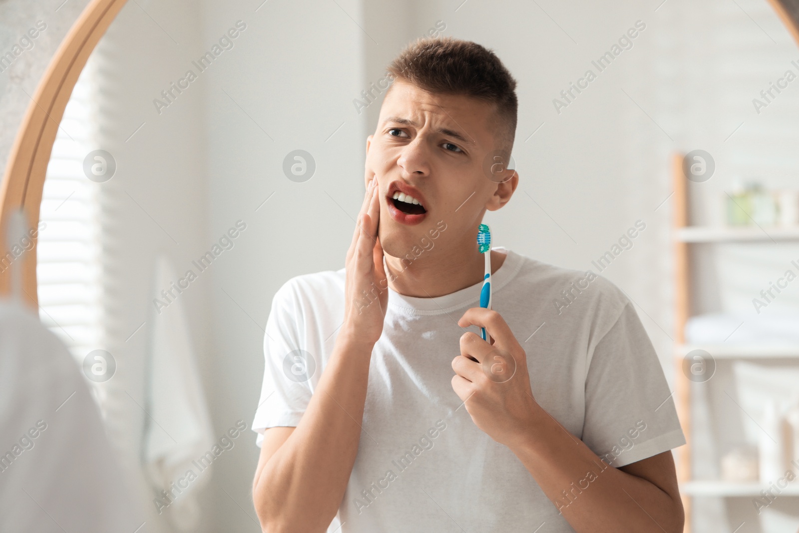 Photo of Young man with toothbrush suffering from toothache in bathroom