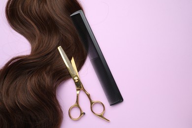 Photo of Brown hair strand, comb and professional scissors on violet background, top view. Space for text