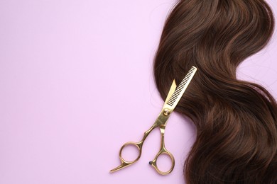 Photo of Brown hair strand and professional scissors on violet background, top view. Space for text