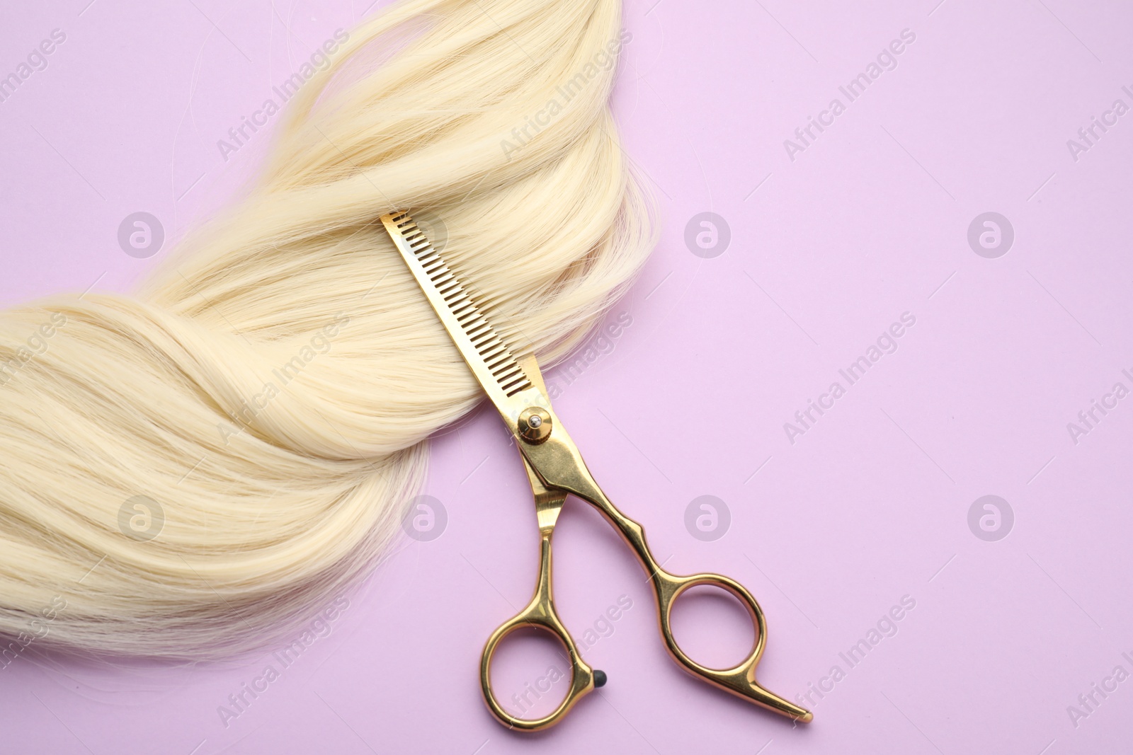 Photo of Blonde hair strand and professional scissors on violet background, top view. Space for text