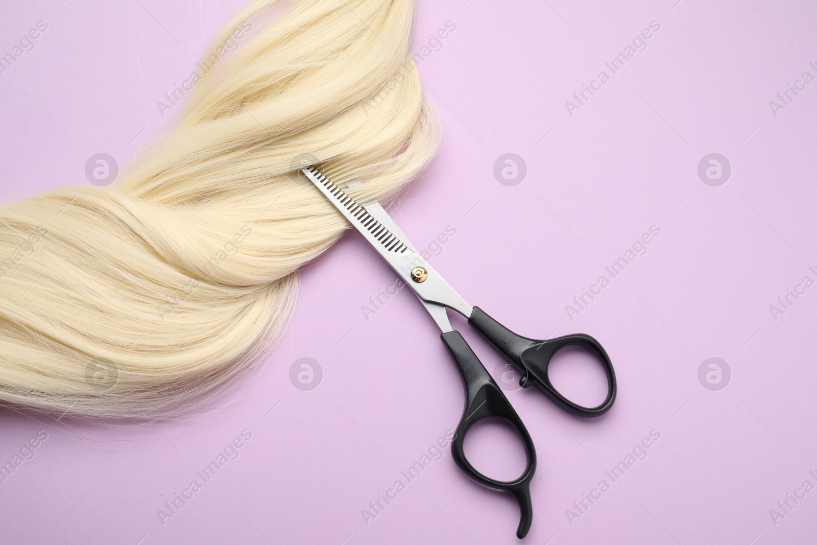 Photo of Blonde hair strand and professional scissors on violet background, top view