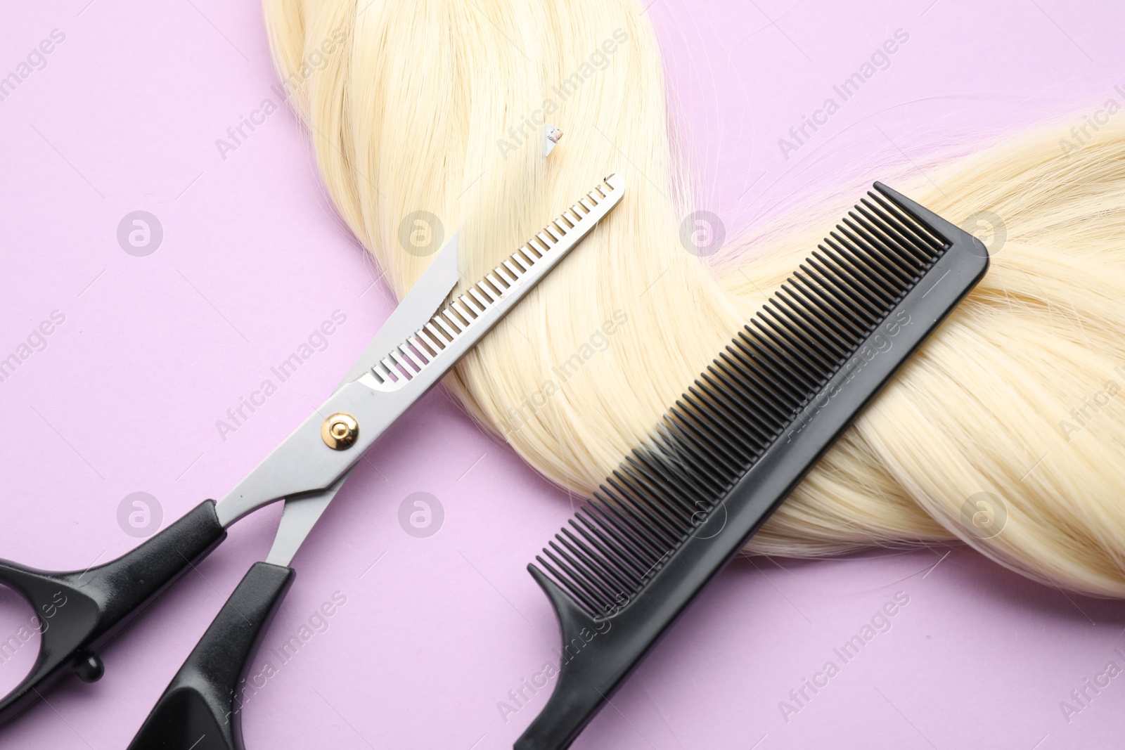 Photo of Blonde hair strand, comb and professional scissors on violet background, top view